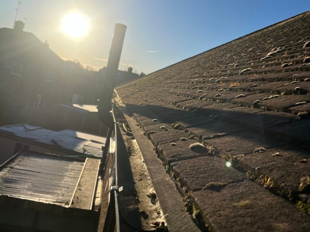 Professional gutter cleaning in progress on a residential tiled roof with moss buildup.