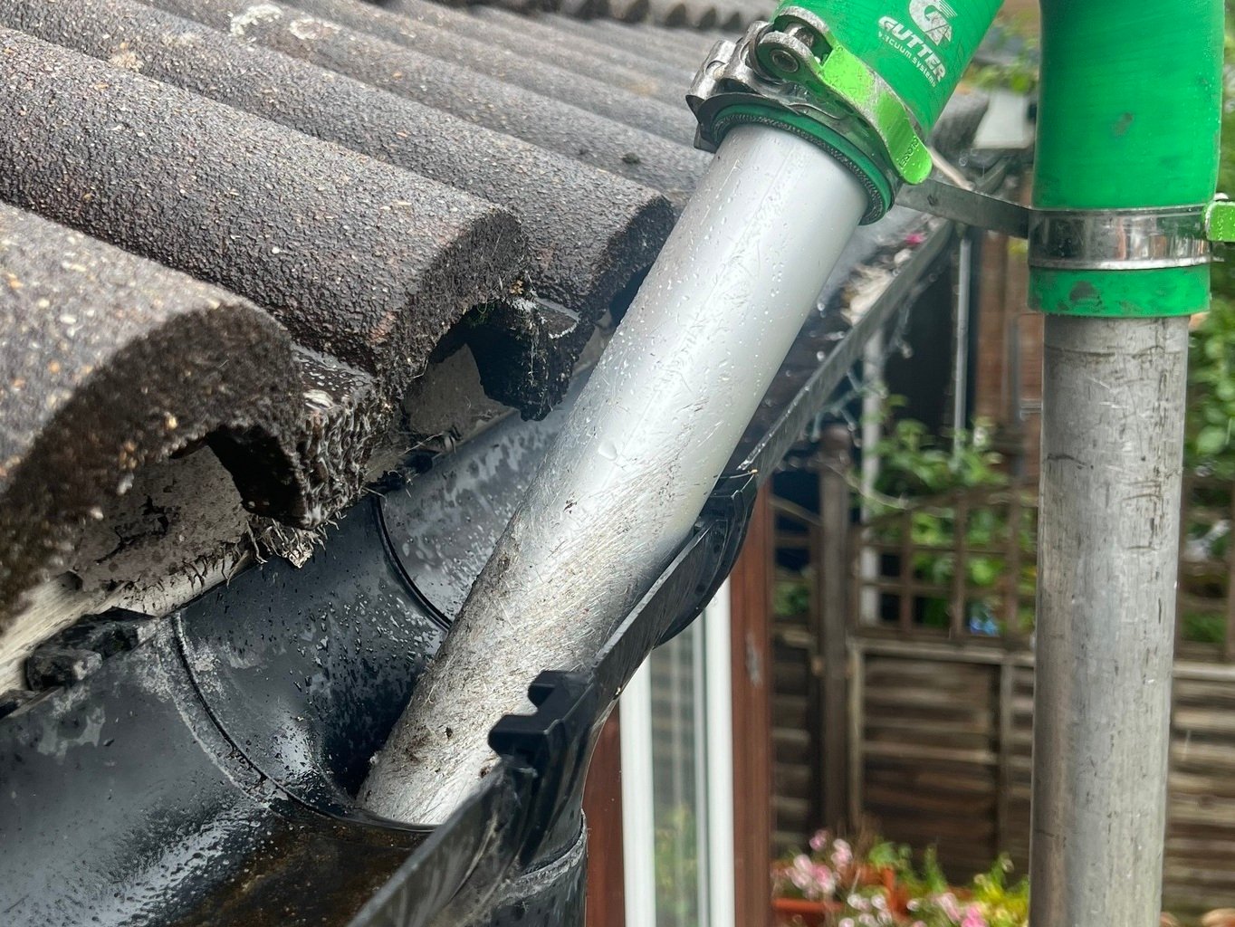 Technician using a high-reach gutter vacuum system to clean a blocked downpipe and gutter on a residential property.